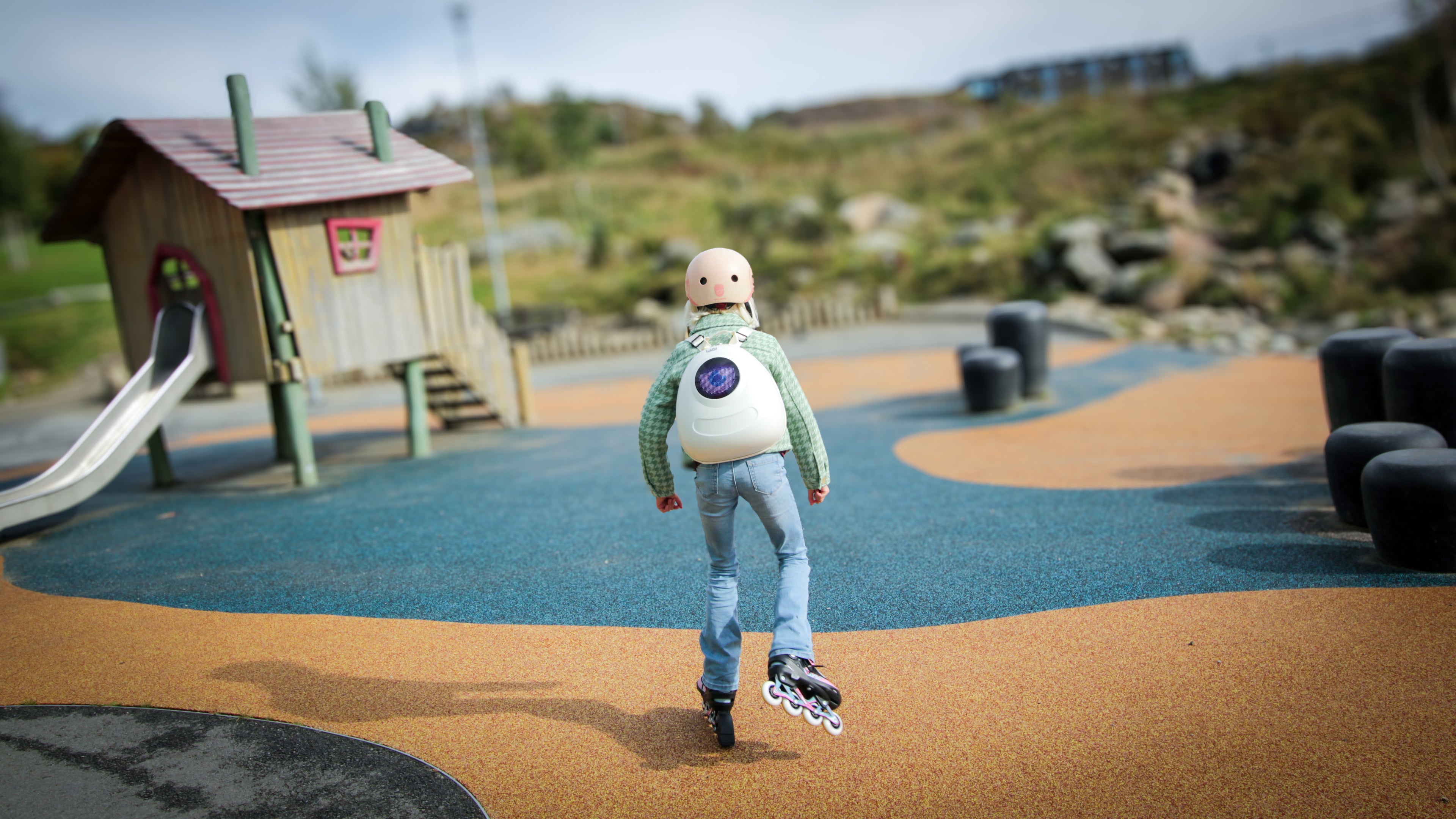 Action shot of a girl on roller skates skating towards a playground, wearing a Whipped Cream White Ledback Buddy backpack, against a blurry background of a playground with a playhouse with a slide in the background.